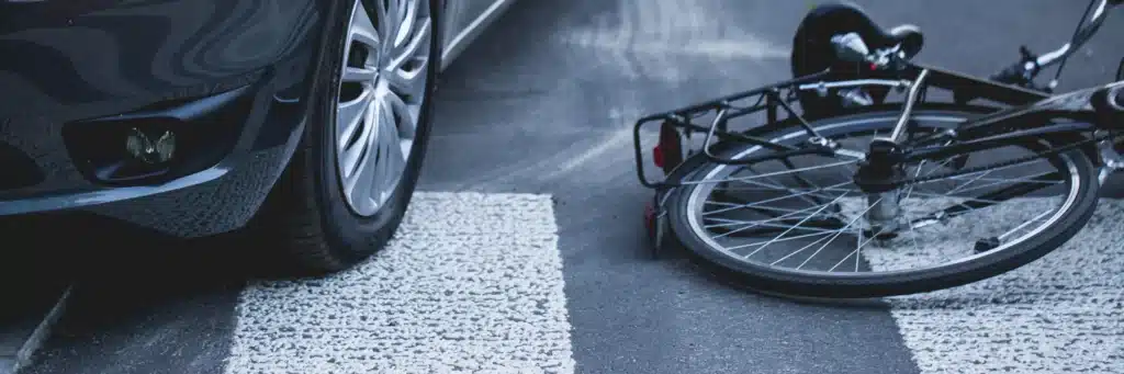 Bicycle laying on ground next to car in crosswalk