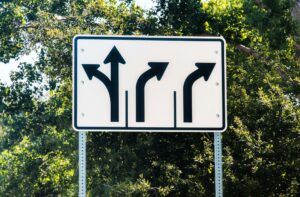 A white traffic sign with black arrows informing drivers of the left, straight, and right turn lanes