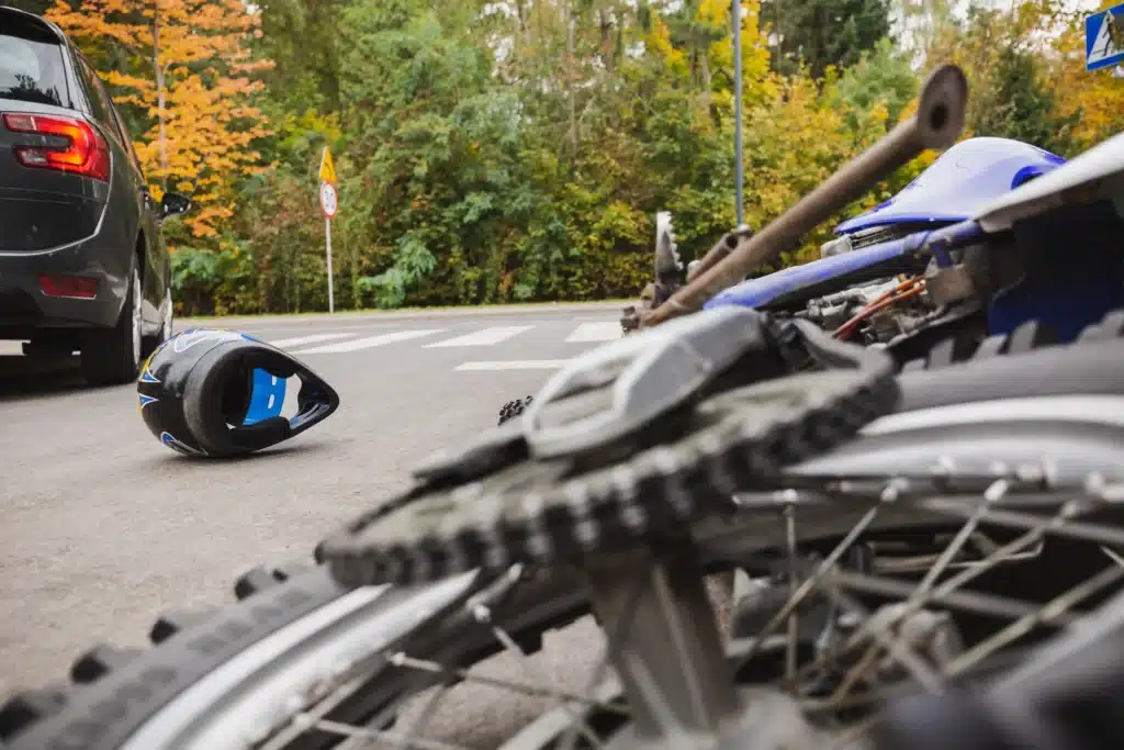 Motorcyle laying on ground with helmet next to it with a car in front