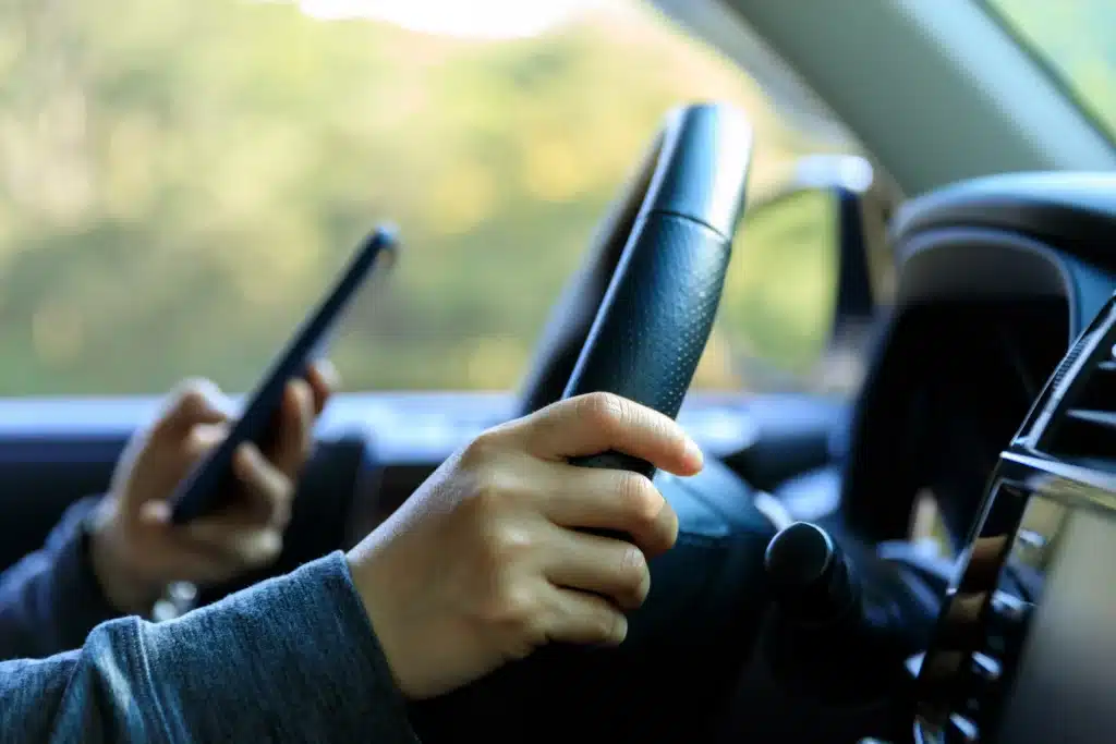 Closeup of hands on steering while while one holding a phone
