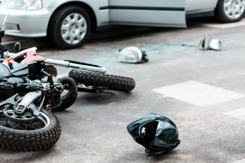 Motorcycle, helmet, and part laying on street next to car